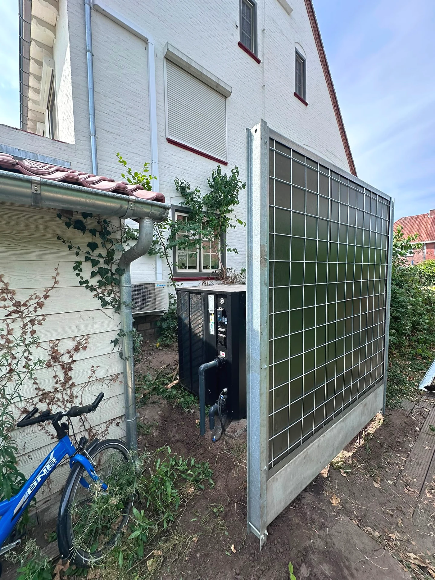 Zijaanzicht van het Noise-Reducer scherm en de warmtepomp naast de woning