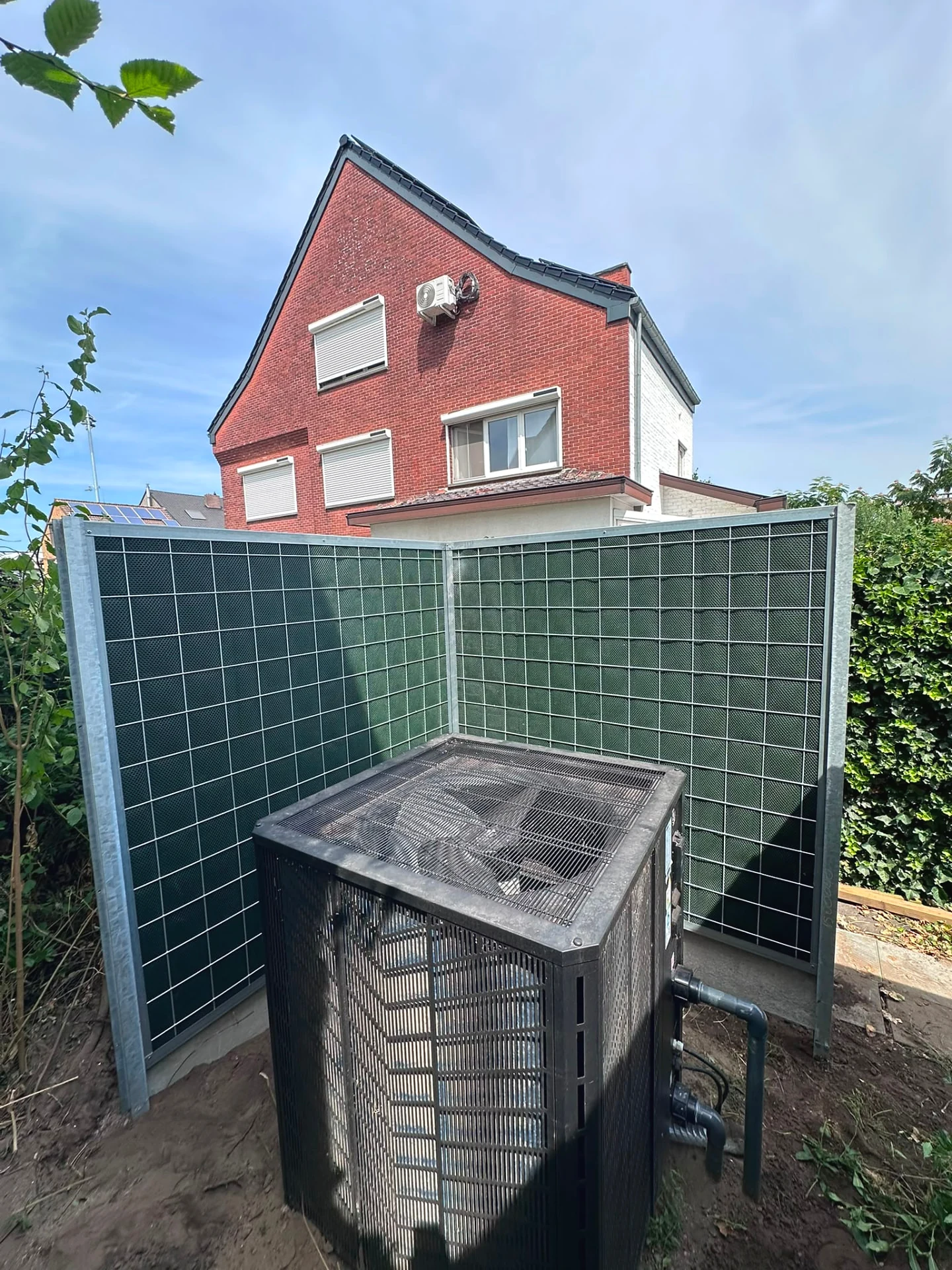 Noise-Reducer scherm rond een warmtepomp op de grond naast een woning
