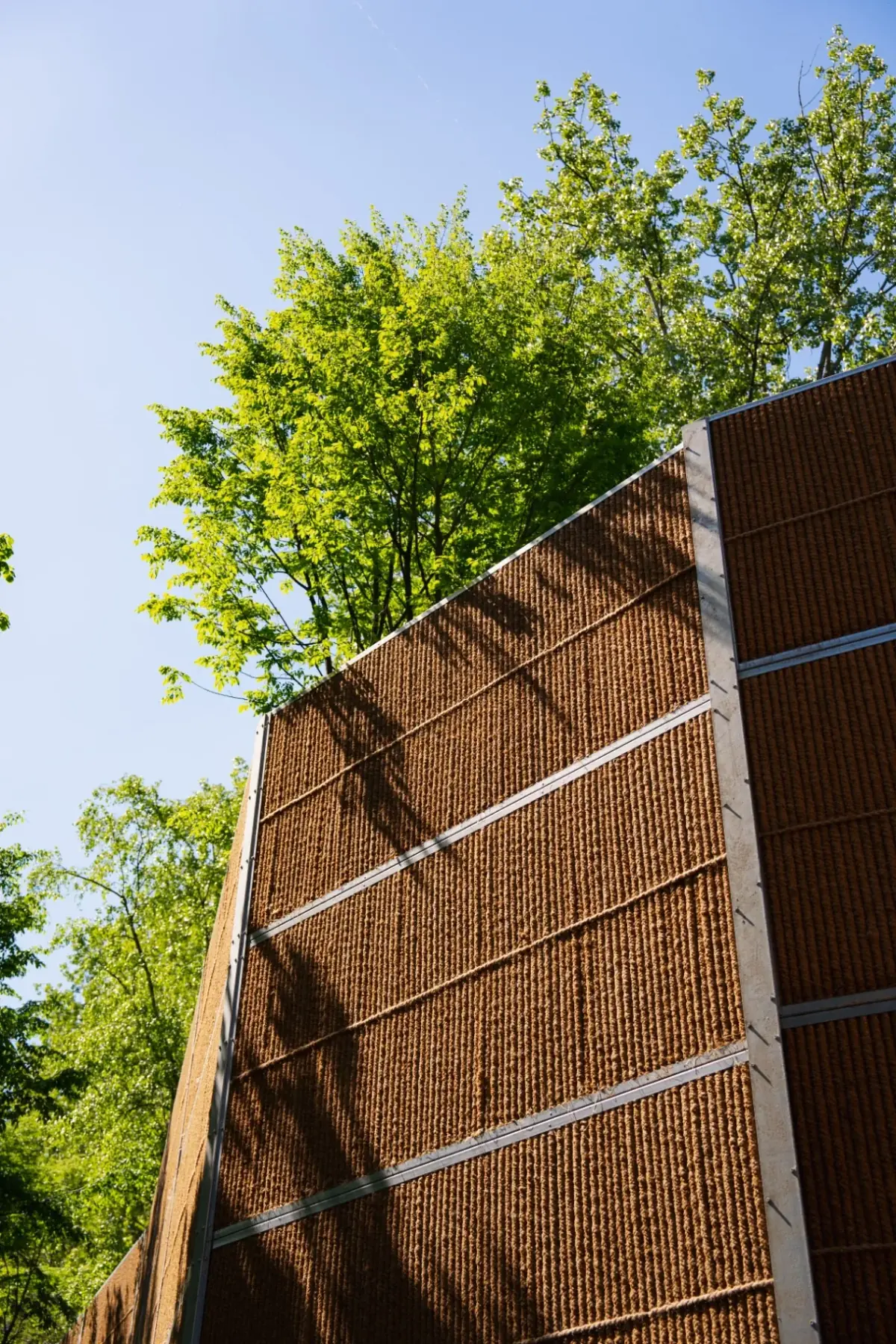 Haut écran anti-bruit Kokowall avec structure en fibre de coco naturelle entre des arbres, conception en pente ascendante