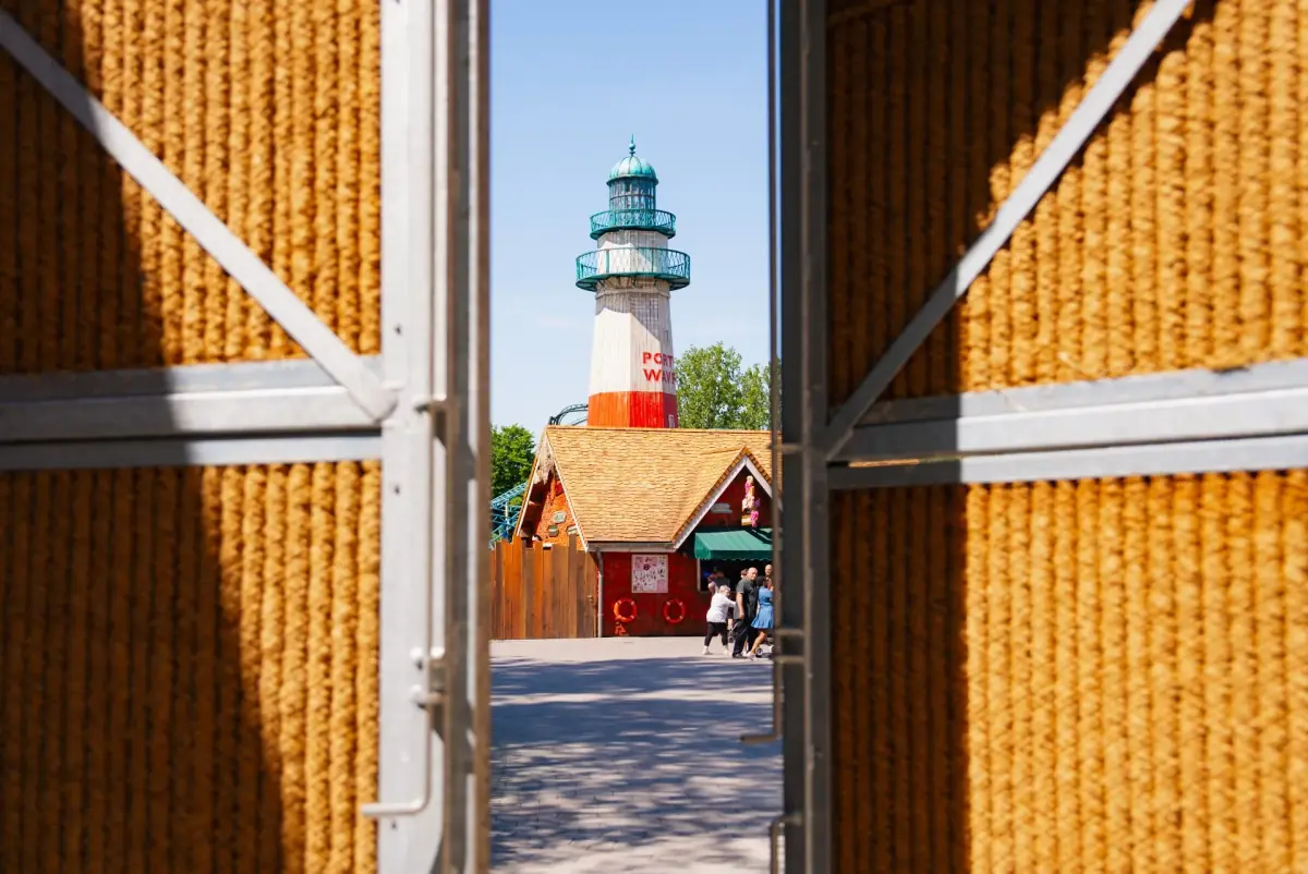 Écran anti-bruit Kokowall avec une ouverture de porte donnant sur le parc d'attractions Plopsaland, avec un phare en arrière-plan