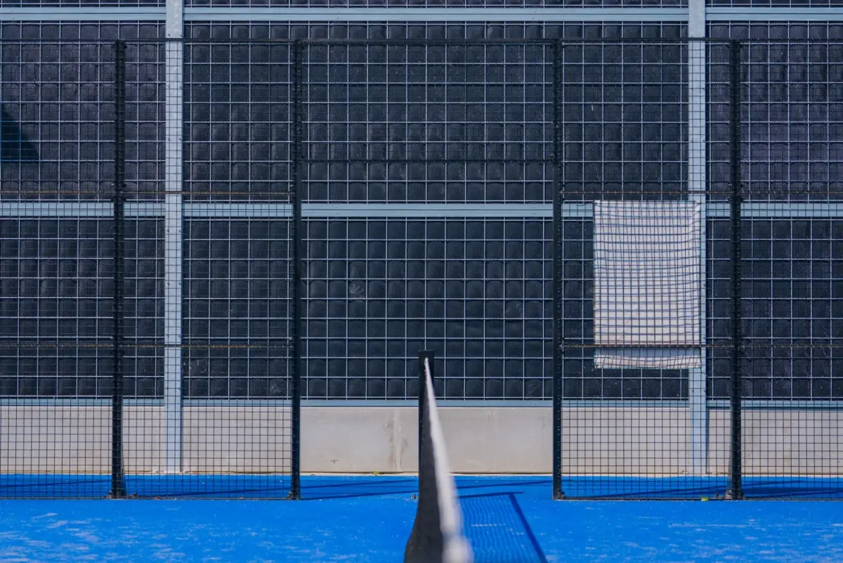 Noise-Reducer industrial sound barrier around a padel court, with dark grey panels behind the mesh fence